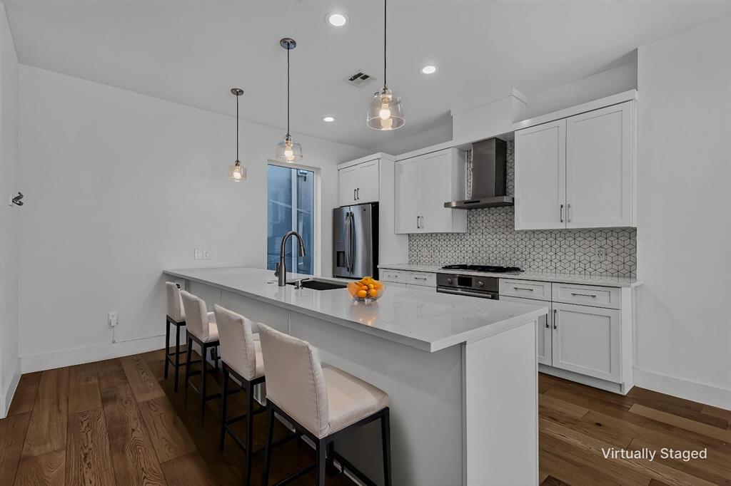 Kitchen featuring white shaker-style cabinetry, quartz countertops, patterned tile backsplash, stainless steel appliances, and wood-finish flooring