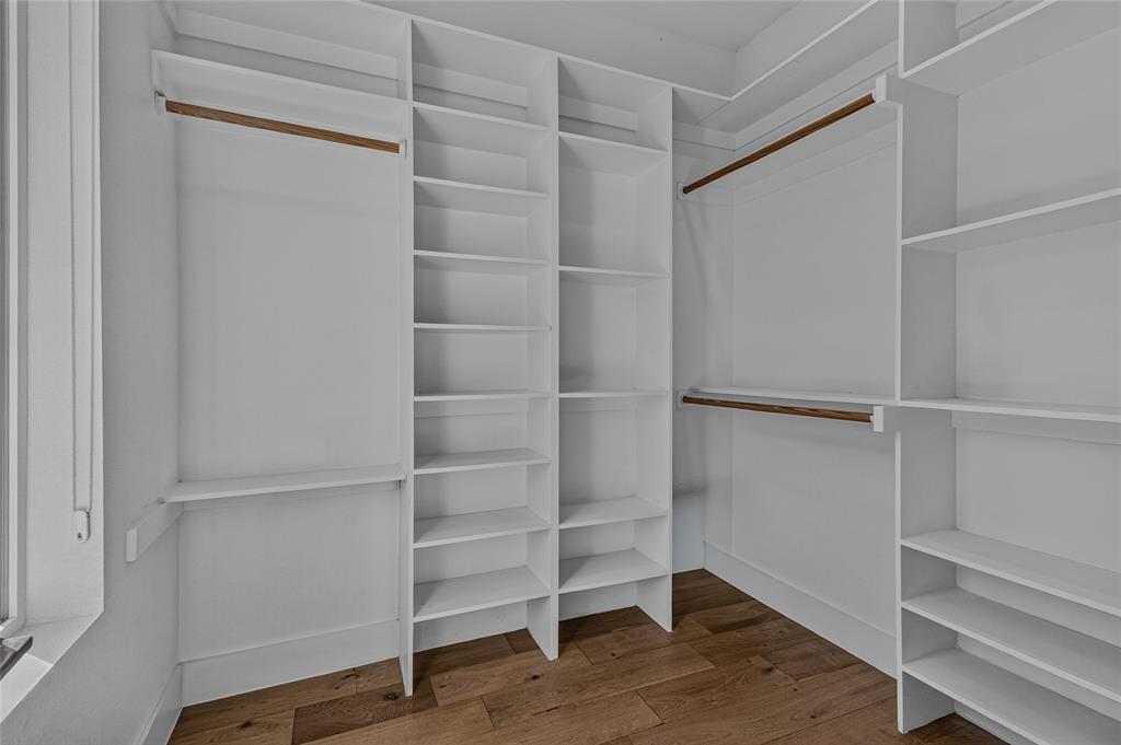 Primary Walk-in closet featuring white built-in shelving, wooden closet rods, and wood-finish flooring