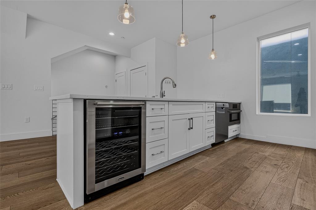 Kitchen island featuring white shaker-style cabinetry, an integrated stainless steel wine refrigerator, a high-arc faucet, quartz countertops, and wood-finish flooring