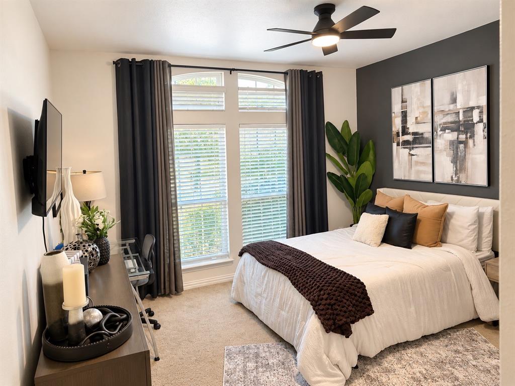 Room featuring neutral carpeting, a dark charcoal accent wall, oversized windows with arched transoms, and a modern ceiling fan with integrated lighting