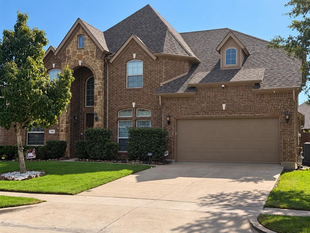 Brick and stone facade featuring a multi-gabled roofline, arched window detailing, and a multi-car garage Brick and stone facade featuring a multi-gabled roofline, arched window detailing, and a multi-car garage
