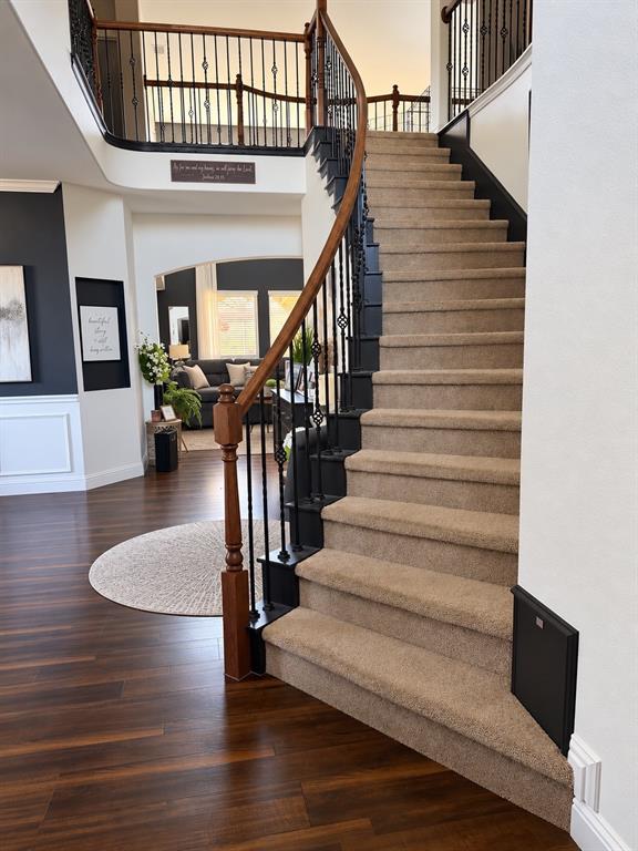 Curved staircase featuring carpeted treads, wood-finish handrails, and metal balusters, complemented by wood-finish flooring and wall wainscoting Curved staircase featuring carpeted treads, wood-finish handrails, and metal balusters, complemented by wood-finish flooring and wall wainscoting