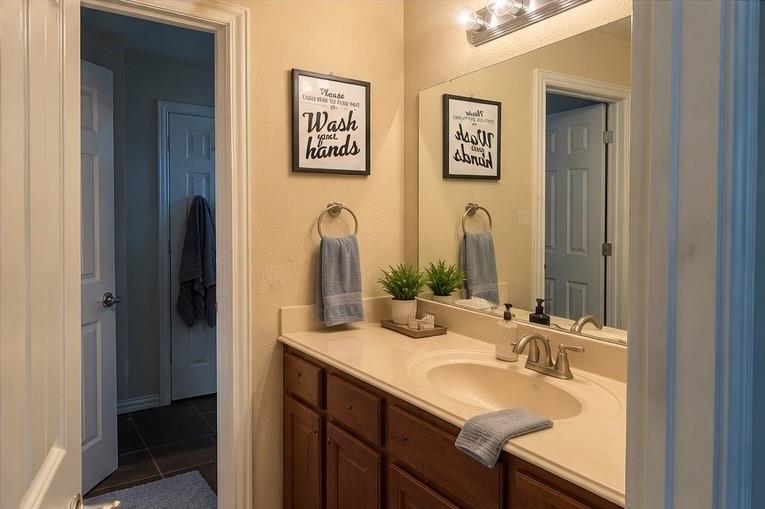 Bathroom vanity featuring dark-tone wood cabinetry, an integrated basin, a polished countertop, a large wall-mounted mirror, and multi-bulb vanity lighting