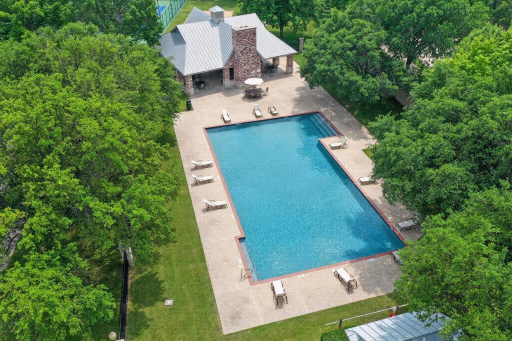 Rectangular community  swimming pool with stone decking, a stone masonry fireplace, a covered pavilion, and surrounding mature trees