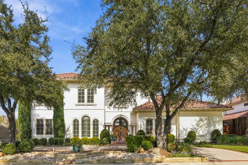Mediterranean-inspired exterior featuring stucco facade, terracotta tile roof, arched entryway with decorative wood doors, multi-pane arched windows, and mature shade trees Mediterranean-inspired exterior featuring stucco facade, terracotta tile roof, arched entryway with decorative wood doors, multi-pane arched windows, and mature shade trees