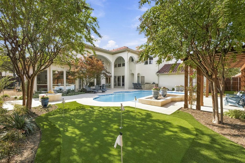 Backyard oasis featuring an in-ground pool, built-in putting green, stone-finished fire pit, putting green, covered pergola, and arched stucco exterior architecture