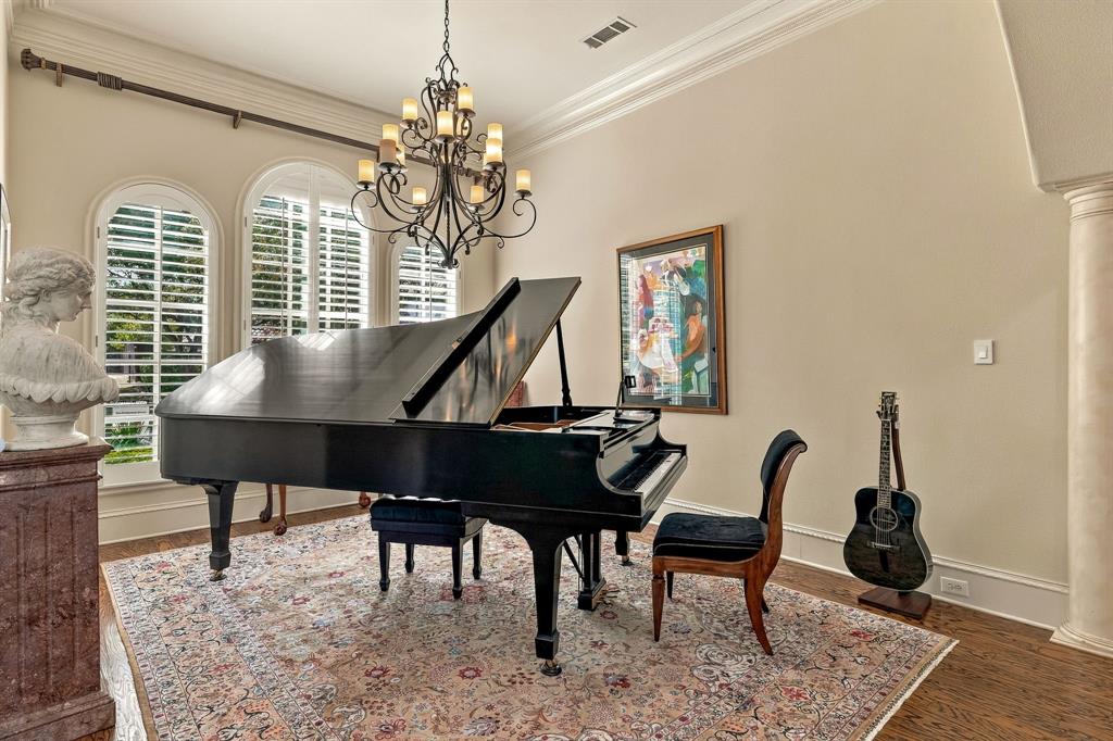 Arched windows with interior shutters, crown molding, wood-finish flooring, decorative column, and a multi-tiered metal chandelier