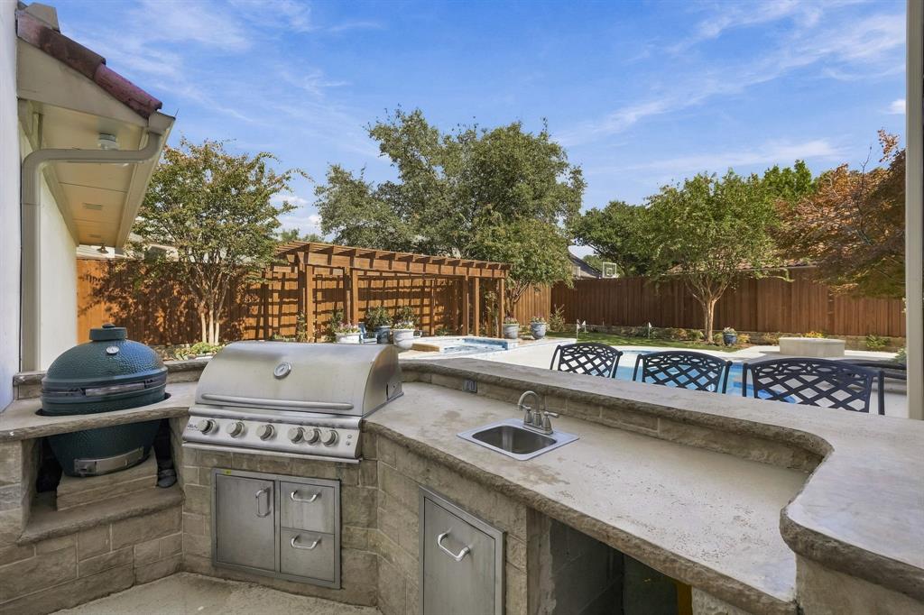 Outdoor kitchen featuring a stainless steel grill, drop-in basin, and built-in ceramic kamado-style cooker, overlooking an in-ground pool and wood-framed pergola
