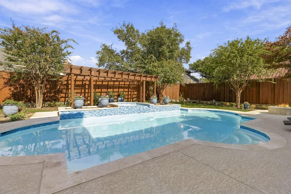Inground swimming pool with tiled water feature, integrated spa, wood-slat pergola, and concrete decking