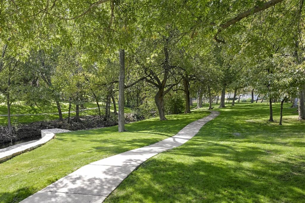 Expansive grounds featuring mature shade trees, a winding concrete pathway, stone retaining wall, and a natural creek border