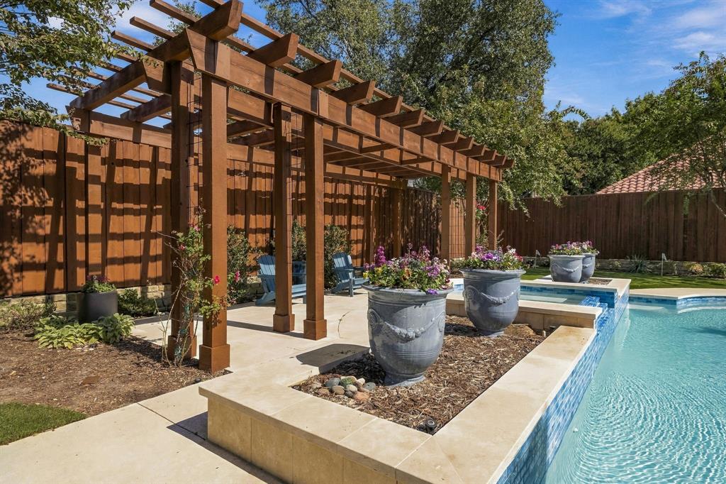 Outdoor living space featuring a stained-wood pergola, natural stone pool decking, and an elevated stone planter border