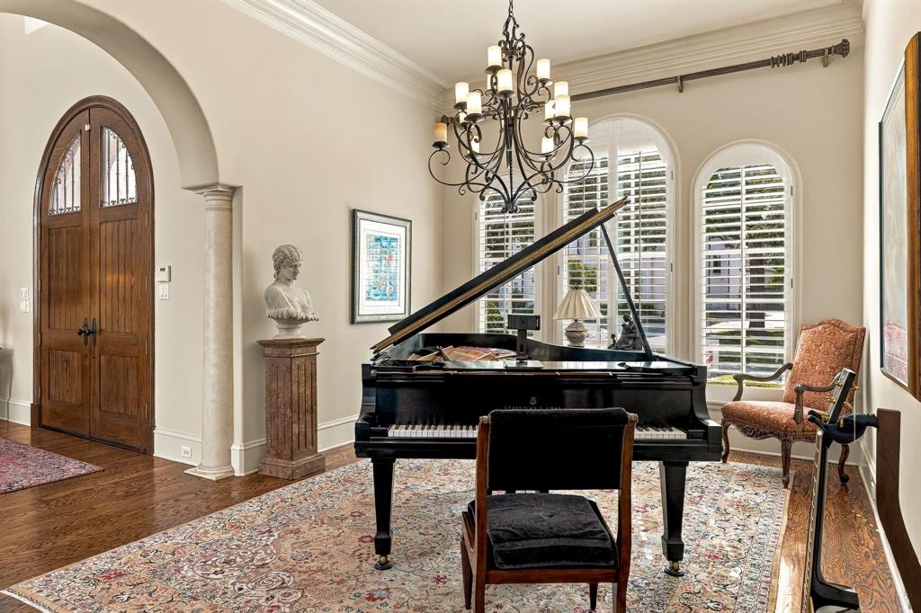 Classic crown molding, wrought iron multi-arm chandelier, and arched windows with plantation shutters