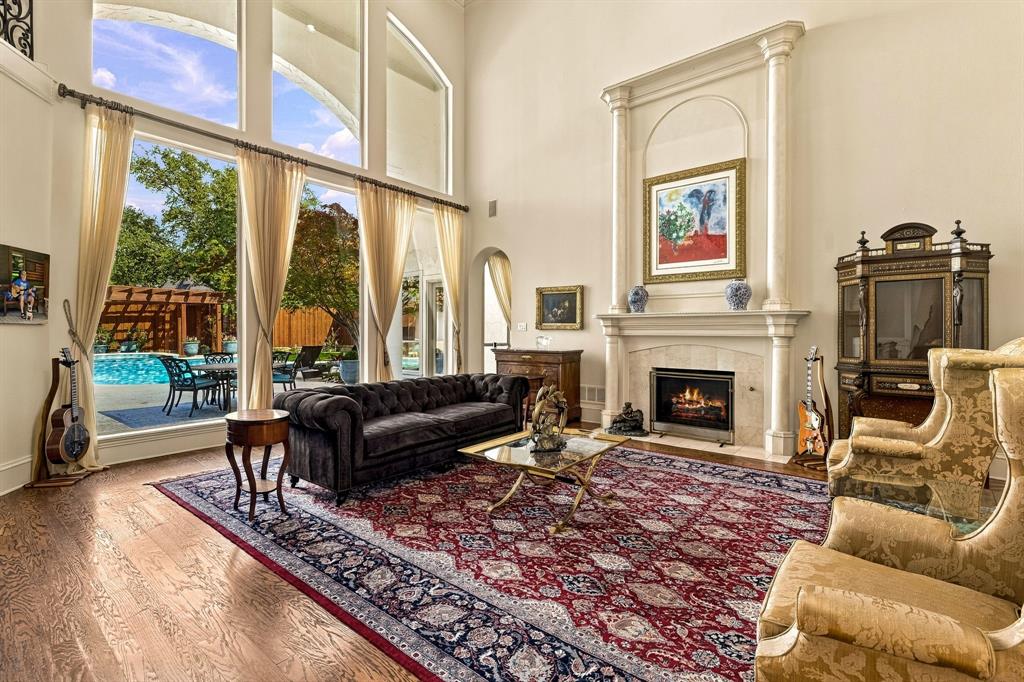 Vaulted ceilings, expansive floor-to-ceiling windows, wood-finish flooring, and a fireplace with a decorative stone mantle
