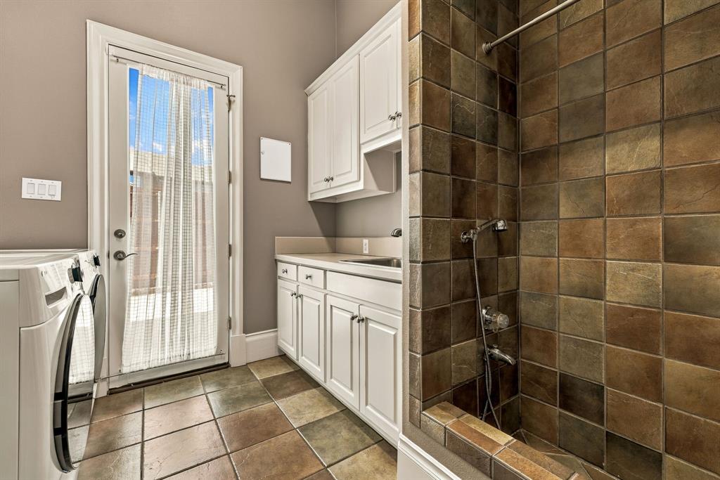 Utility area featuring white built-in cabinetry, an integrated sink with a solid-surface countertop, tile flooring, and a tiled shower stall