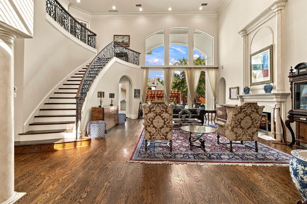 Grand foyer featuring high ceilings, arched windows, wood-finish flooring, a curved staircase with ornate iron railings, and a fireplace with a decorative mantel