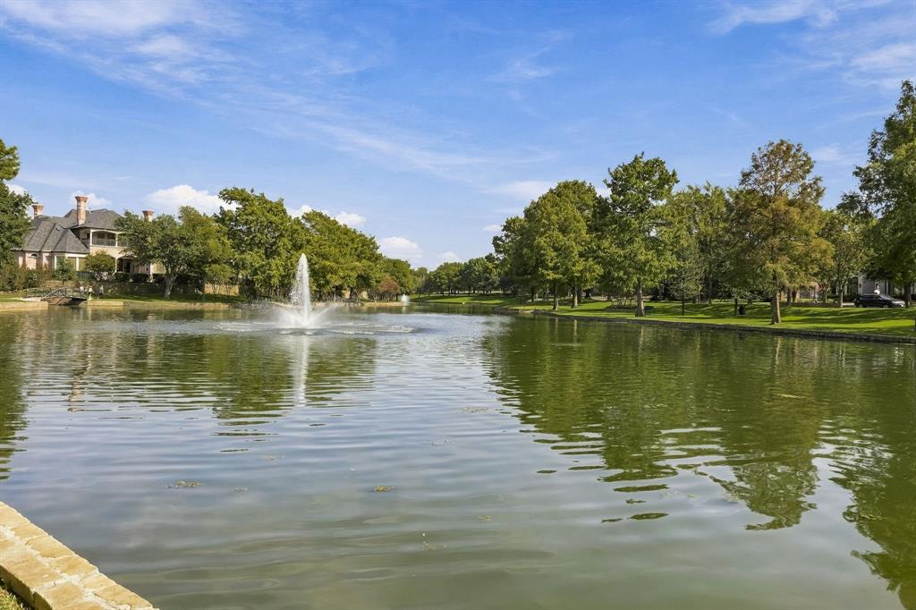 Water feature with a central fountain, expansive pond, stone-edged shoreline, and mature trees