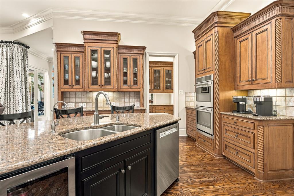 Kitchen featuring medium-toned wood cabinetry with decorative crown molding, stone countertops, stainless steel dual-wall oven, integrated dishwasher, and wood-finish flooring