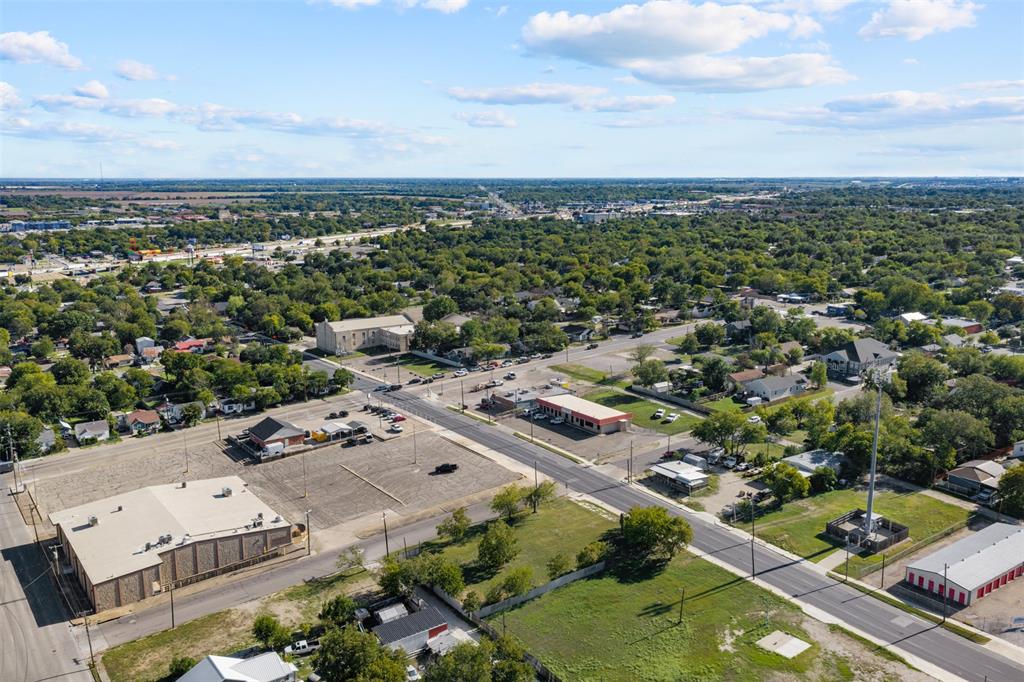 Aerial view of an urban landscape featuring paved roadways, commercial structures, expansive parking lots, and established tree canopy