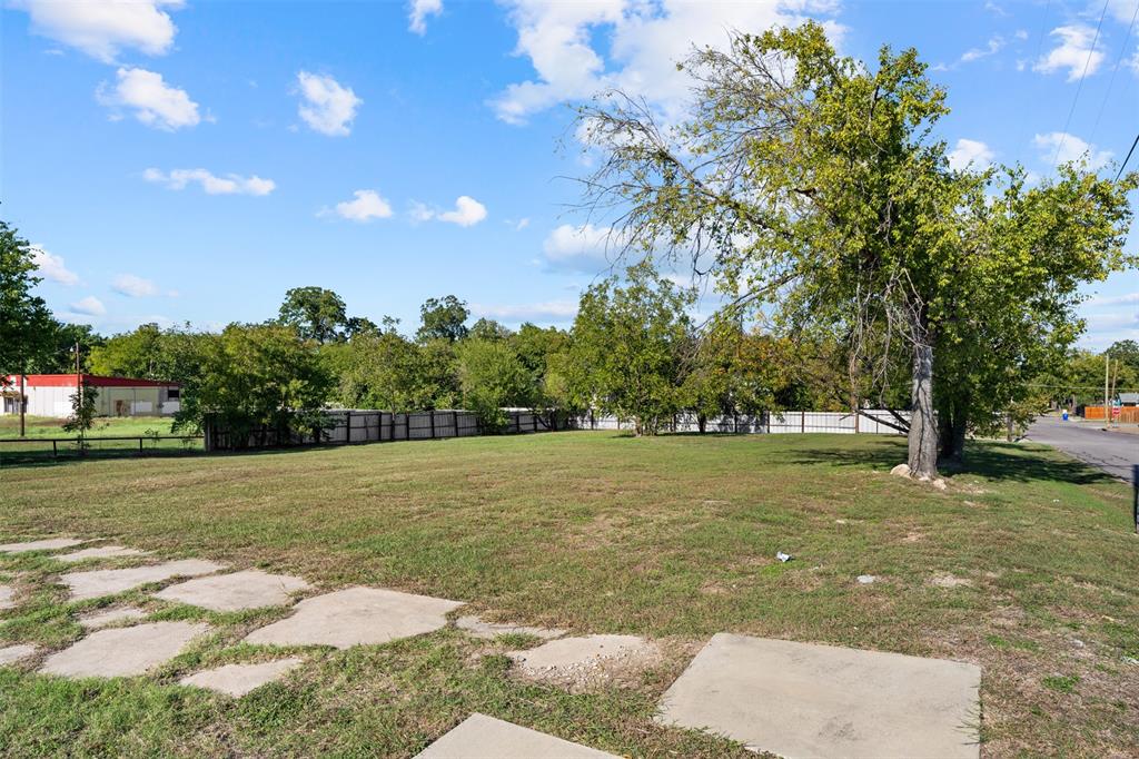 Expansive open lot featuring a level grass expanse, mature trees, and perimeter wood-slat fencing