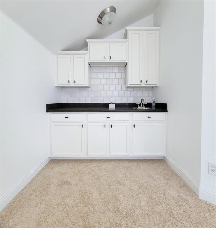 Built-in cabinetry featuring white Shaker-style doors, dark stone-finish countertops, a subway tile backsplash, and a stainless steel sink with a dual-handle faucet