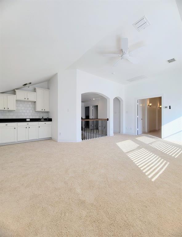 Vaulted ceilings, built-in cabinetry with stone-finish countertops, subway tile backsplash, and decorative archways with a metal balustrade
