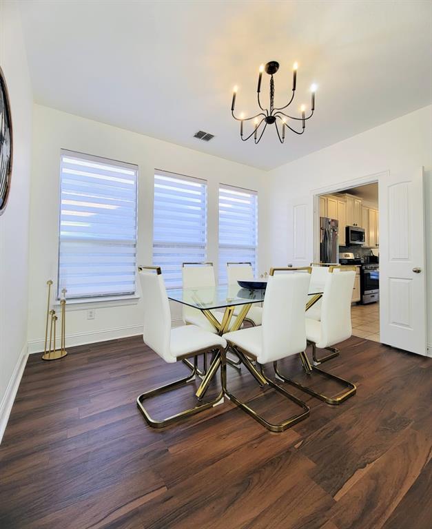 Dining area featuring wood-finish flooring, a multi-arm chandelier, and three large windows with adjustable blinds Dining area featuring wood-finish flooring, a multi-arm chandelier, and three large windows with adjustable blinds