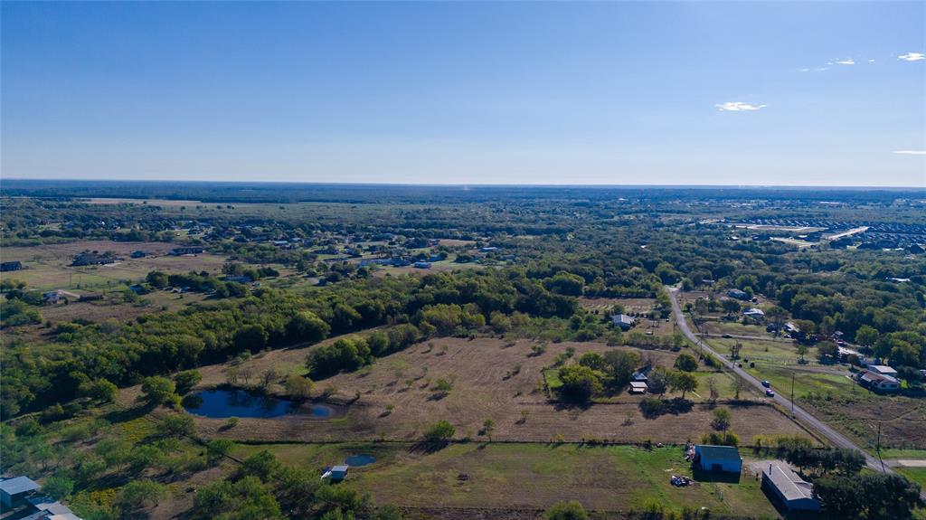 Aerial perspective of expansive acreage featuring a pond, mature trees, and cleared pasture land