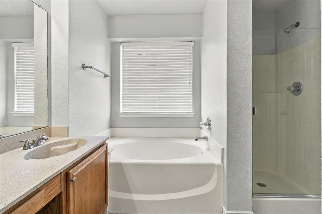 Bathroom featuring a wood-finish vanity with an integrated sink and countertop, a soaking tub, and a glass-enclosed shower with a chrome fixture