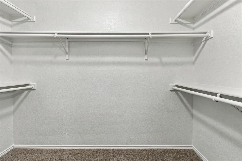 Storage area featuring white wire shelving units, dual-level hanging rods, and neutral carpeting