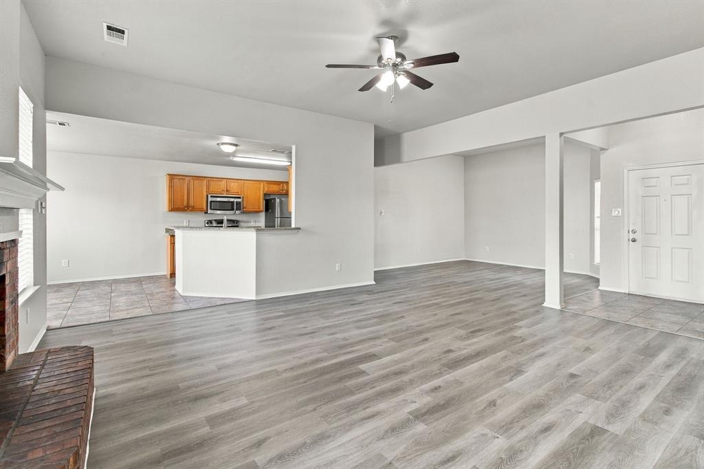 Open-concept interior featuring wood-finish flooring, a brick fireplace hearth, and a kitchen with built-in wooden cabinetry, stainless steel appliances, and a breakfast bar