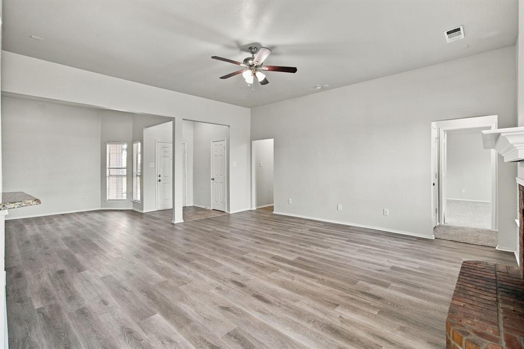 Open interior space featuring wood-finish flooring, vaulted ceilings, a central ceiling fan with integrated lighting, and a brick fireplace hearth