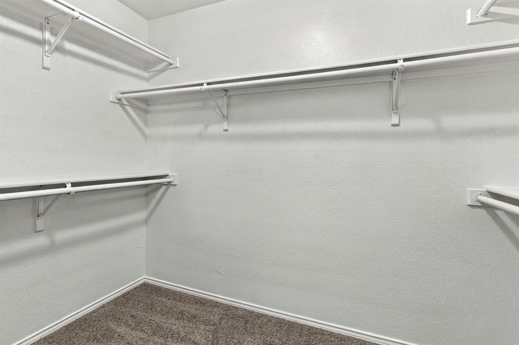 Walk-in storage space featuring multi-level white shelving and integrated clothing rods with textured wall finish and wall-to-wall carpeting