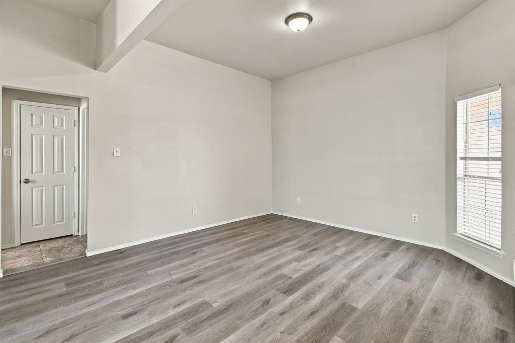 Interior space featuring wood-finish flooring, high ceilings, a flush-mount ceiling light fixture, and a single-panel interior door Interior space featuring wood-finish flooring, high ceilings, a flush-mount ceiling light fixture, and a single-panel interior door