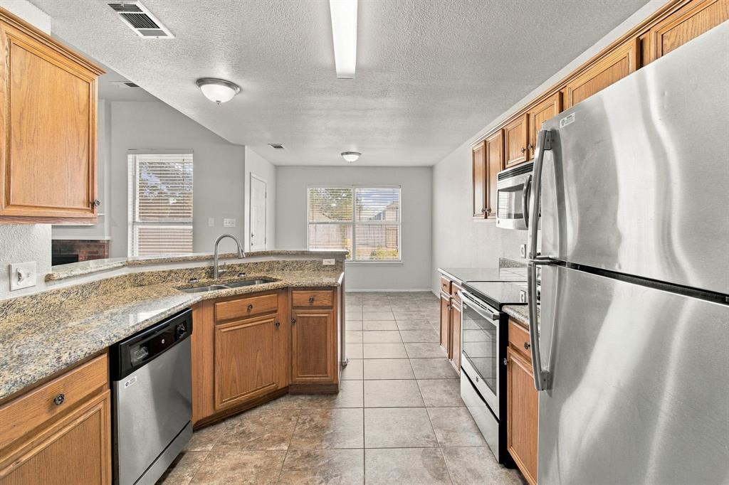 Kitchen featuring cabinetry, stone-finish countertops, stainless steel appliances, and tile flooring
