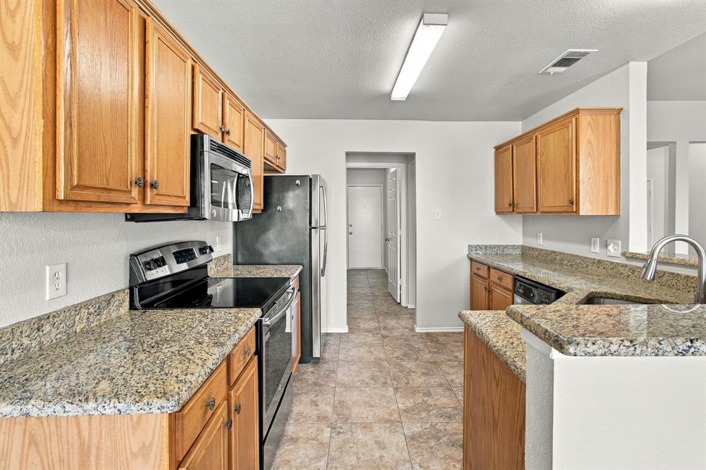 Kitchen featuring medium-tone wood cabinetry, stone-surface countertops, tile flooring, and stainless steel appliances
