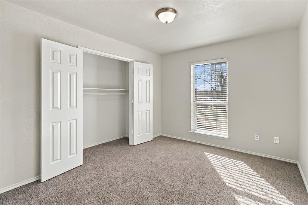 Neutral wall tones, wall-to-wall carpeting, window with slatted blinds, and double-door closet with built-in shelving