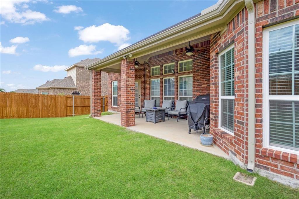 Expansive green lawn with a covered patio featuring brick columns, concrete flooring, and multiple ceiling fans