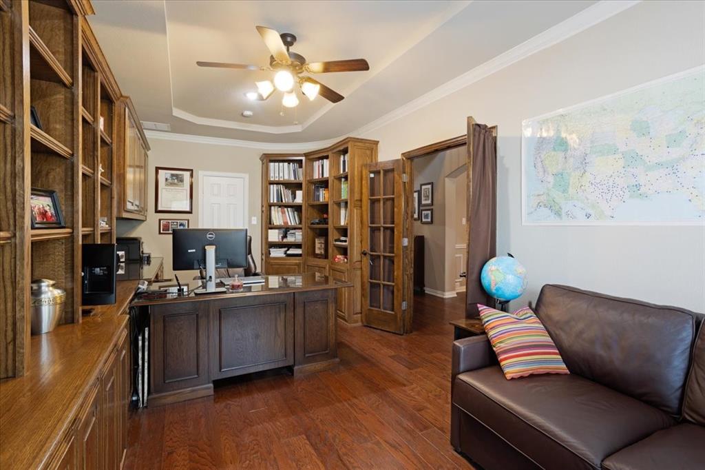 Home office featuring extensive built-in wood cabinetry, wood-finish flooring, a tray ceiling with a ceiling fan, and French doors