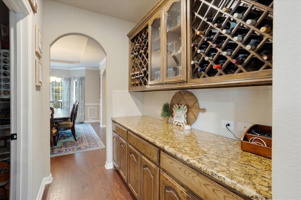 Built-in wine storage cabinetry with glass-front display, substantial countertop space, wood-finish flooring, and an arched doorway framing a dining area