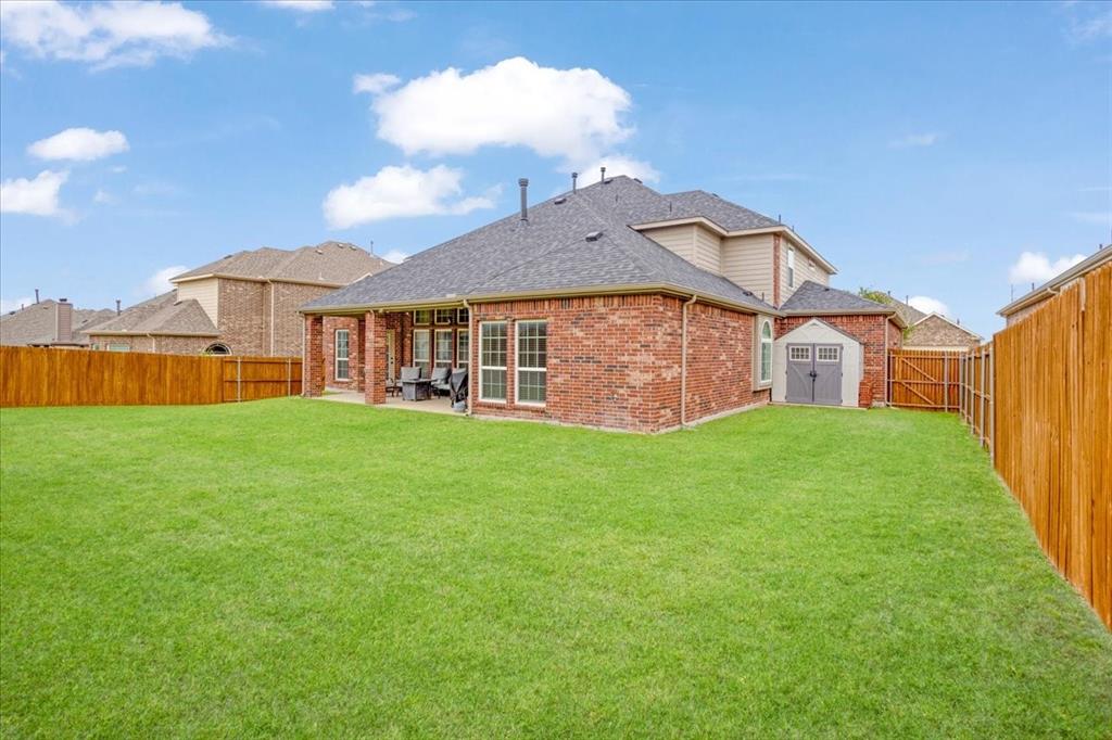 Expansive backyard featuring a lush lawn, privacy fencing, and a covered patio