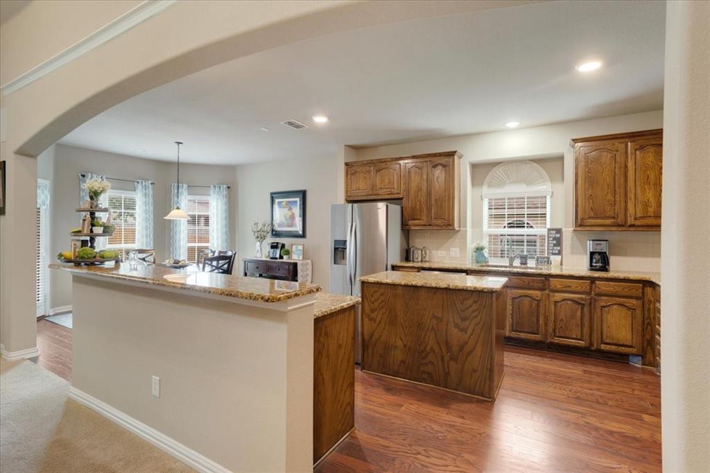 Open-concept kitchen with wood-finish flooring, granite countertops, wood cabinetry, a central island, and stainless steel appliances