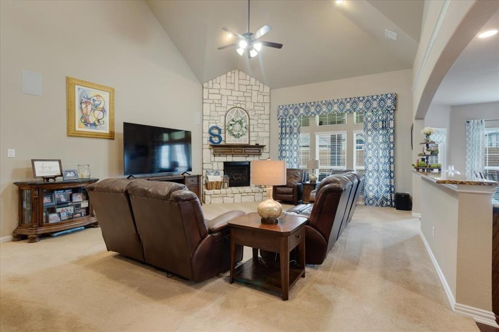 Living area featuring a stone fireplace, vaulted ceiling with a ceiling fan, and large windows
