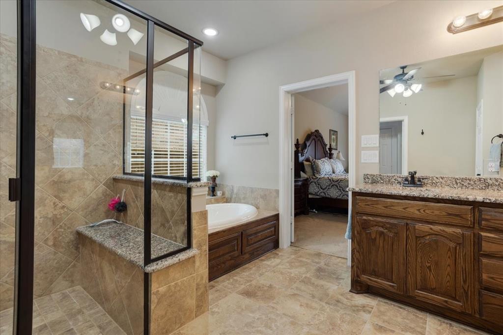 Spacious bathroom featuring a glass-enclosed shower with a built-in bench, a jetted soaking tub, a double vanity with granite countertop, and tiled flooring