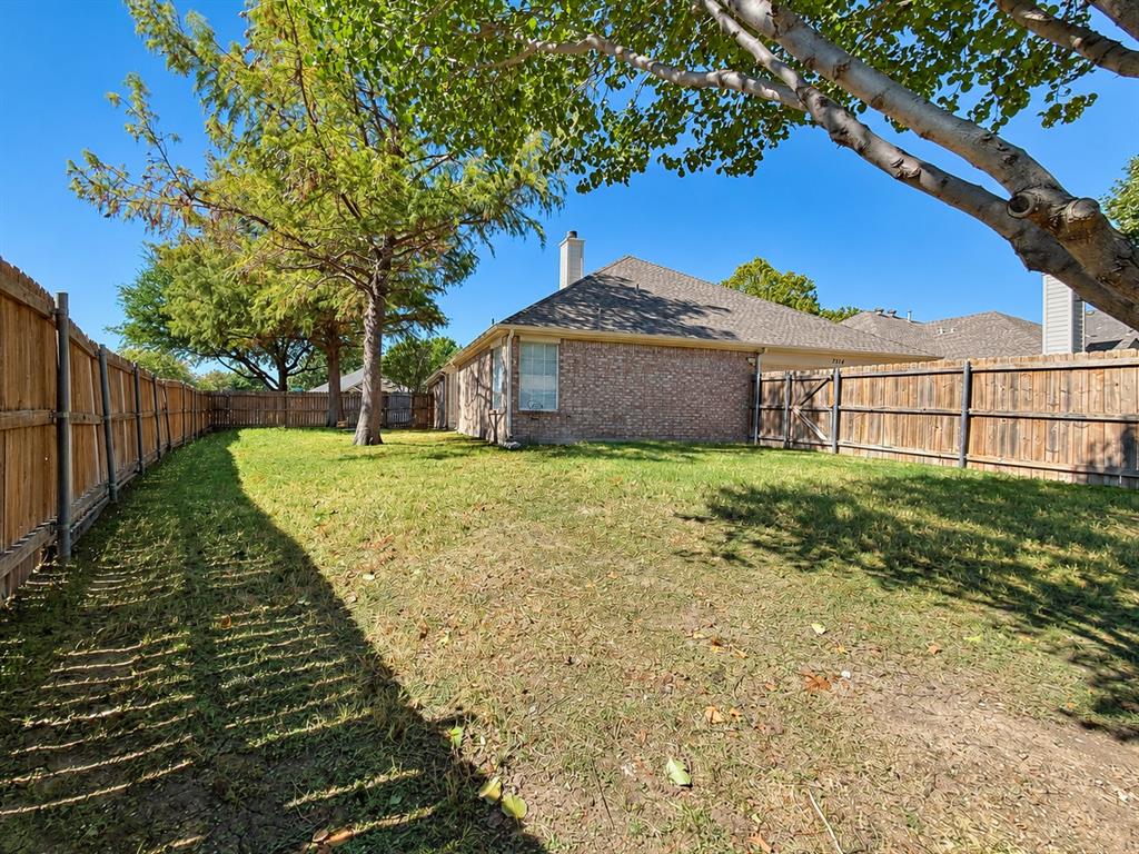 Fenced backyard featuring a brick exterior, shingle roof, chimney, and mature trees