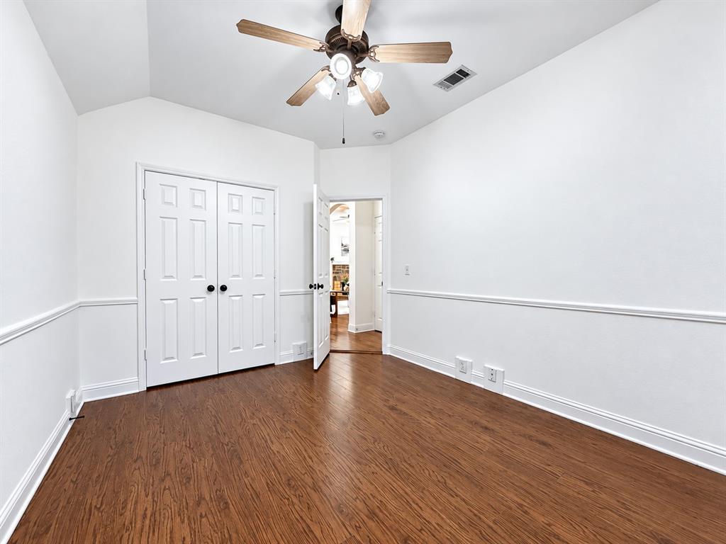 Room featuring wood-finish flooring, a vaulted ceiling, double-panel closet doors, chair rail molding, and a ceiling fan with integrated lighting