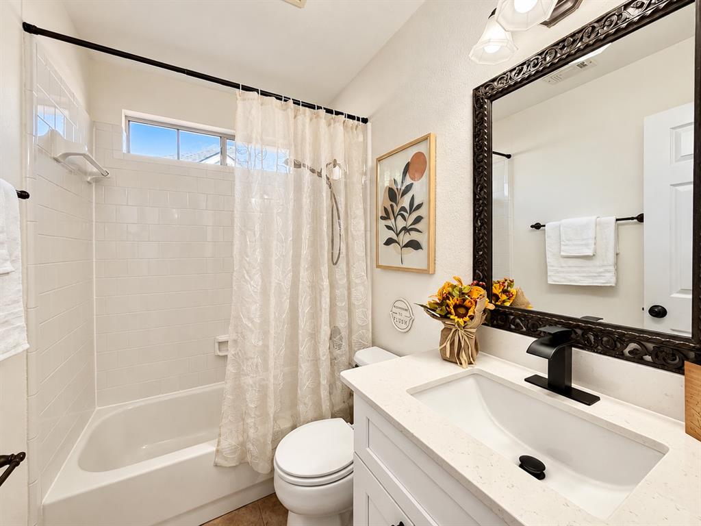 Bathroom featuring a vanity with a white countertop and rectangular undermount sink, matte black faucet, framed mirror, and a tub-shower combination with white wall tile