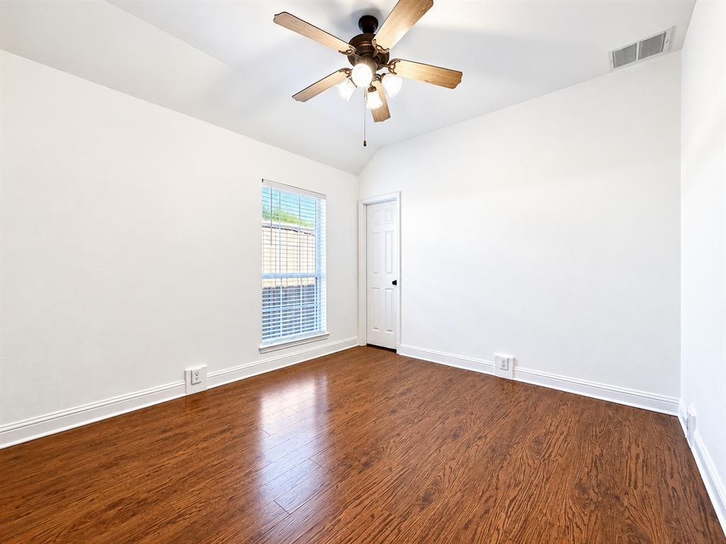Vaulted ceiling room featuring wood-finish flooring, a central multi-blade ceiling fan with integrated lighting, and a single-panel interior door