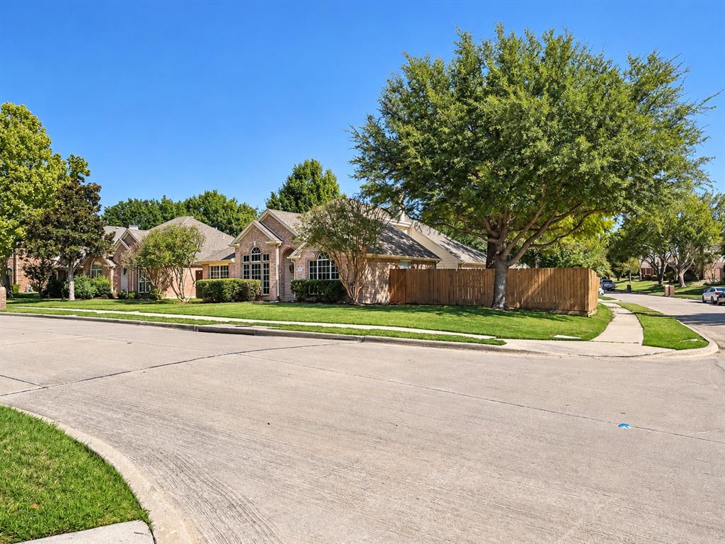 Corner lot residence featuring a brick facade, arched window detailing, wood-finish privacy fencing, and mature trees
