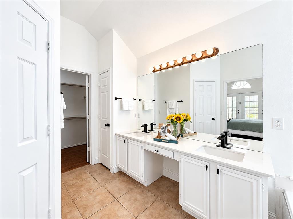Dual-sink vanity with white cabinetry, expansive countertop, matte black fixtures, and a multi-bulb vanity light