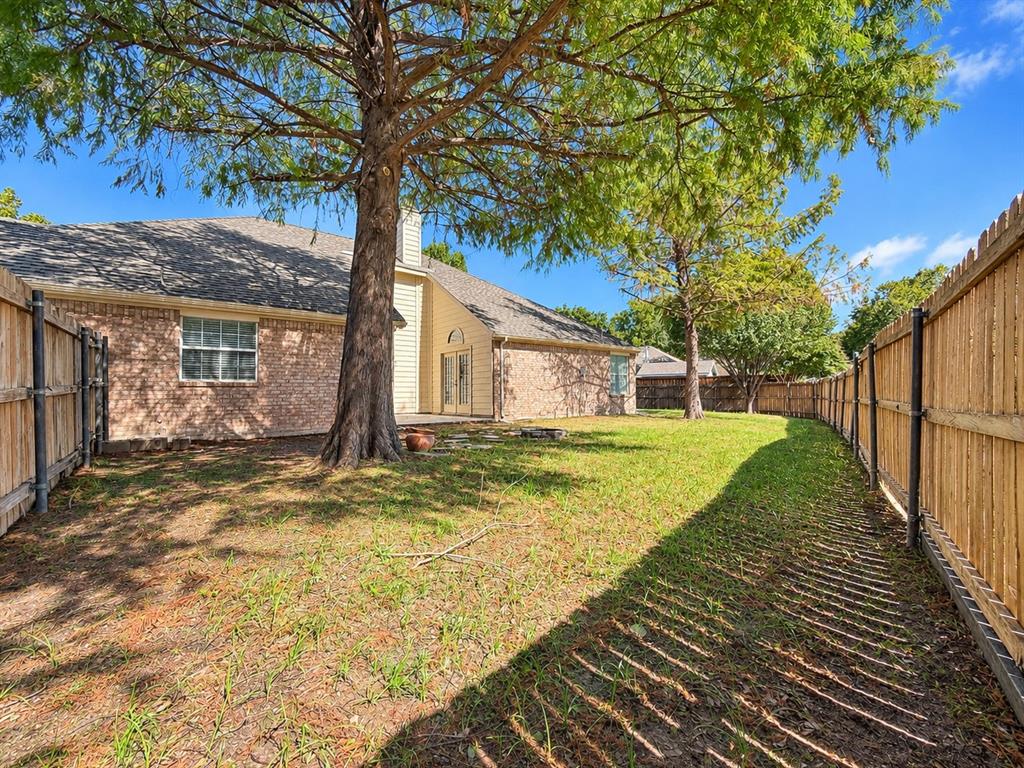 Spacious backyard featuring masonry exterior siding, mature trees, and wooden privacy fencing
